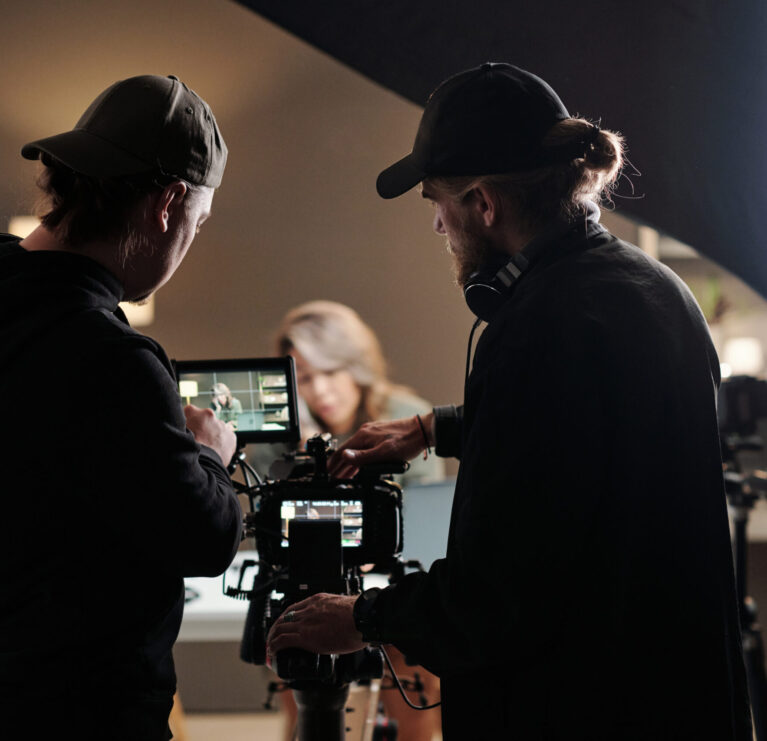 Back view of two young men standing in front of camer aand using steadicam while shooting new commercial with female model